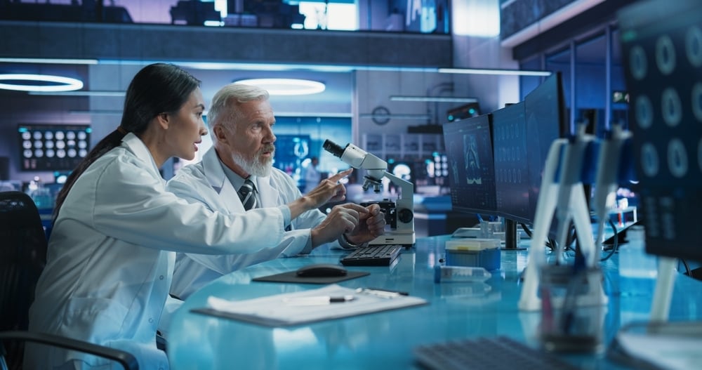 Biotechnology Medical Research Center: Female Neuroscientist Using Desktop Computer And Talking To Male Doctor With Microscope.