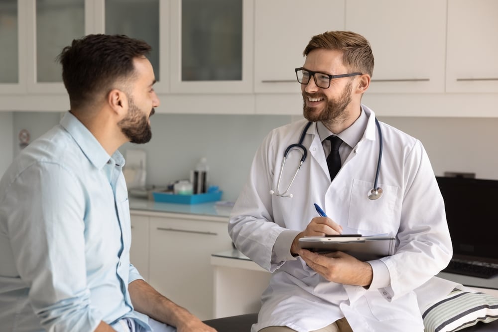 Positive doctor filling up medical card during conversation with patient in modern examination room.